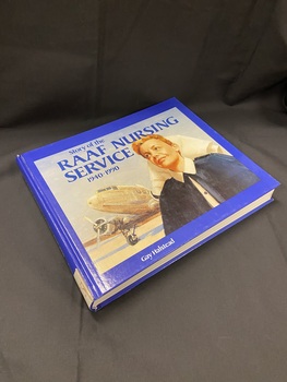 Royal blue hardcover book with white printed title on the spine. The front cover has a rectangle template covering most of the cover, inside which is an image of a nurse with aplane on the runaway behind her. The title is printed across the top of the image in blue text. The author's name is printed in white at the bottom of the cover, below the rectangle image.