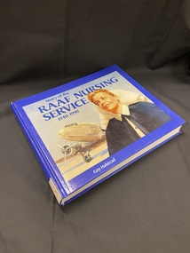 Royal blue hardcover book with white printed title on the spine. The front cover has a rectangle template covering most of the cover, inside which is an image of a nurse with aplane on the runaway behind her. The title is printed across the top of the image in blue text. The author's name is printed in white at the bottom of the cover, below the rectangle image.