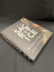 Large hardcover book with a black cover. The title and the author's name are printed in large white letters on the spine and on the front cover. The title on the cover is printed in large text across four rows in the centre of the space, the first line reads THE ART OF, then the word SACRIFICE is broken into three sections with three letters of the word on each line, the first letter i in sacrifice has been replaced with a crucifix. On the right edge of the cover is a painted partial image of a person's head and shoulders wearing a military hat.