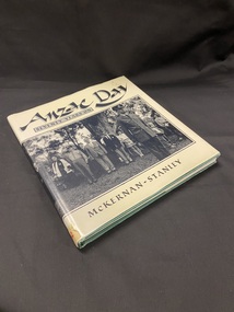 Green hardcover book with cream coloured dustjacket. There is a black and white photo that wraps around the whole dustjacket depicting a crowd at a Memorial Service in Toronto, New South Wales. On the front section of the dustjacket the title is printed above the photo and the author is printed below, both in black print.