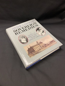 Dark blue hardcover book with a grey dustjacket. The title and author details are printed along the spine in black text. The cover has the author's name acrsoo the top in purple print, followed by a black line and then the title in large black print and another balck line. Beneath this are two oval templates with photographs of a nurse in each one and the subtitle is written between the two. At the bottom of the cover is a drawing of the Ballarat Hospital from the early 1900s.