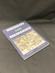 Dark blue softcover book. Title and author printed along spine in white print. Front cover has white and green print and a black and white image of Prisoner Of War medical personnel operating on a patient, watched over by soldiers.