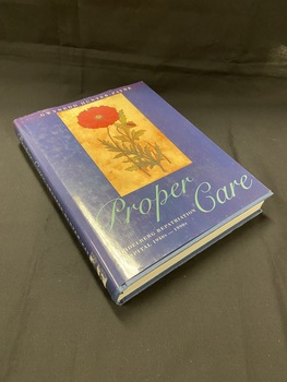 Hardback book with a dark blue dustjacket. Along the spine the title is printed in light aqua script, followed by the printed text of the sub-title and author's name, there is a mark on the bottom of the spine where a sticker has previously been removed.
The front shows an image of a red flower with some greenery set in a light brown rectangle, below which the title is again printed in light aqua script.