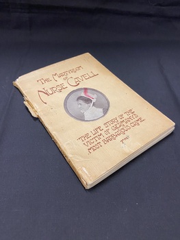 Small, worn paperback book with a faded and discoloured cream cover that is torn along the spine. There is a portrait of Nurse Cavell in a round template in the centre of the cover and the title and sub-title are rinted above and below the image in brown print.