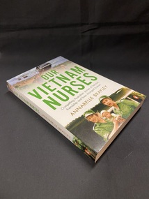 White cover with title printed in green text across the front, subtitle and author's name below in balck and brown print. The top of the cover shows a photo image of a helicopter landing in a field, followed by two more in the distance and soldiers on the ground. Another photo image at the bottom of the cover shows two females in army greens holding a baby.
The images and text appears the same way on the spine of the book.