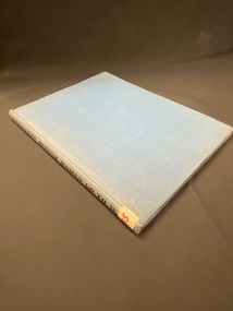 Faded blue clothbound hardcover book. The title is printed in black along the spine and there is a white sticker with B55 written in red ink taped to the bottom of the spine.