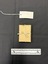 Small light brown cardboard box tied with natural coloured cotton string. This photograph is taken upon a black background, with a scale card and object number included.