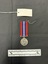 Front view of the War Medal 1939-1945. The silver coloured medal has a central and textured design of the crowned effigy of King George VI, facing left, around the perimeter is the legend 'GEORGIVS VI D:G:BR:OMN:REX ET INDIAE IMP:' The ribbon is coloured in vertical strips: red, blue, white, red, white, blue, red, it is tactile, feeling ribbed under finger. This photograph is taken upon a black background, with a scale card and object number included.