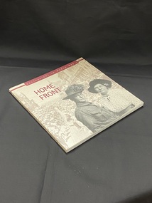 Square shaped paperback book with a sepia toned, faded image of a military parade down a city street lined with people. The image wraps around both covers and the spine. Title printed in burgundy print along the spine. The front cover has a black and white image in the foreground of a soldier standing with an older woman. There is a burgundy text box across the top with the sub-heading printed inside.