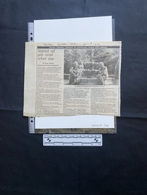 A large newspaper clipping with a title, subtitle, byline, three columns of text and a large black and white photo