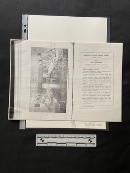 Photocopy of pages from a book that has been copied in landscape orientation to show two pages on one sheet of paper. 
The left side page is a black and white photo displayed sideways of a hospital ward. There is a row of 5 beds along both side walls and a large space in the middle with a small table holding a flower arrangement. Eight of the beds have patients sitting up smiling towards the photographer, there are also five nurses standing beside various beds.
There is a bold black line down the middle of the page and on the right there is a rectangle border around a heading and eleven short paragrphs of black print.
