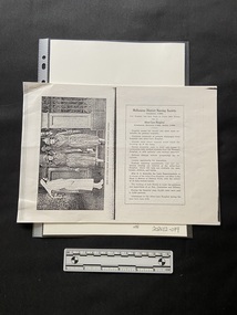Photocopy of pages from a book that has been copied in landscape orientation to show two pages on one sheet of paper.
The left side page is a black and white photo displayed sideways of a nurse dressed in white standing aside so four nusing sisters wearing hats and coats can exit through an entranceway.
There is a bold black line down the middle of the page and on the right there is a rectangle border around a heading and eleven short paragrphs of black print.