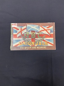 Worn paperback book with two staples down the green spine. The cover background is brown woodgrain, overlain with a large Union Jack covering most of the page. Printed across the bottom of the page is 'it's origin and meaning in olive coloured print.
In the forefront of the Union Jack are three flages (England, Ireland and Scotland) with the title print beneath and two olive brancches.