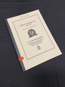 Cream coloured cover with black spine tape. There is a bright orange sticker two inches up from the bottom of the spine with B142 written on it. The front cover has a large double-lined rectangle border around the black printed title. In the centre of the text is the Australia Remembers emblem.