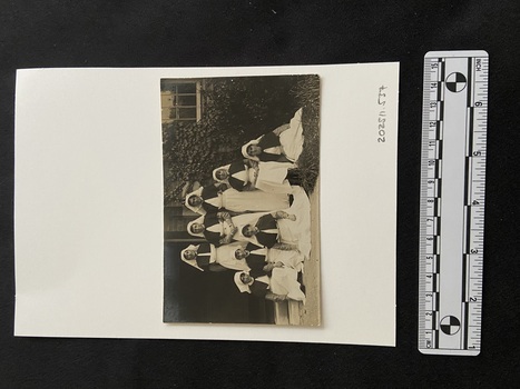Photographic postcard of a group of eight Australian Army Nurses in uniform sitting and standing on the front step of an ivy covered building.