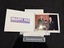 A white card folder each half approximately A5 landscape in size joined on the short edge, opened showing white writing surrounded in purple on the left hand side and a colour photograph of three older people, two men and a shorter woman standing.  The man on the left of the photo is holding an award presenting it to the small woman.  The photo is held in place by white card corners that have purple details and the underneath the photo is the studio logo again.