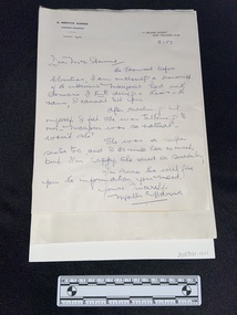 Handwritten letter in blue ink with a letterhead printed in black across the top that reads E. Mervyn Harris. The corresponding address is printed in the top right corner.The letter is attached to backing card. It is lies on top of a pile of typed A4 pages.