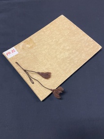 Fawn manilla folder type cardboard cover with a line of ornate embossed pattern running vertically down the left side (two inces in from the spine). Brown thread is tied through the two hole punches on the left side with both ends finished with a knot and tassle.
There is a white sticker label in the top left corner with 'PA32' in red marker.