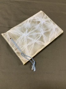Faded dark blue, cloth-bound album, bound with blue rope thread tied into tassles through two eyelets on the cover. There is a lighter blue whispy-lined pattern across the entire cover.