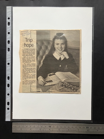 Newspaper clipping with a large black and white portrait photograph of a teenage girl with a book open on the table in front of her.  One column of text on the left.