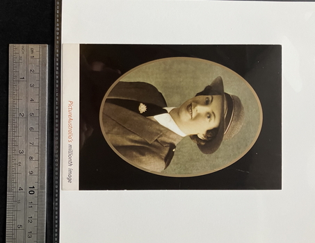 A6 sized postcard on a white background.  Postcard is a colour/sepia toned oval portrait of a woman's head and shoulders wearing an Australian Army Uniform.  The portrait has a gold frame, black behind the frame and caption below the background