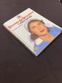 Hardcover book with a light green cover. The Title is printed in red and black. There is a female nurse on the front cover in a blue uniform and white red cross head scarf. The Australian Red Cross symbol is at the top of the front cover.