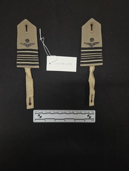 Pair of khaki wool Royal Australian Air Force epaulettes with metal crown and eagle insignia attached via a metal backing plate, three rows of black and khaki braid, and attachment straps with buttonholes.