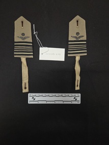 Pair of khaki wool Royal Australian Air Force epaulettes with metal crown and eagle insignia attached via a metal backing plate, three rows of black and khaki braid, and attachment straps with buttonholes.