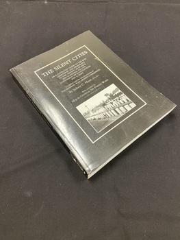 Paperback book with black cover. Title down the spine in white print. Front cover has a white border with title and author details printed inside in white text and a black and white photo of gravesites.