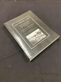Paperback book with black cover. Title down the spine in white print. Front cover has a white border with title and author details printed inside in white text and a black and white photo of gravesites.