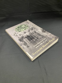 Paperback book with white spine showing title and author and a white sticker at the bottom of the spine with dewey decimal number handwritten on it. The front cover displays a black and white image of nurses and patients standing in a hospital ward. At the top of the page behind the title is another image in an oval template of soldiers resting on the ground.