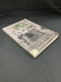 Paperback book with white spine showing title and author and a white sticker at the bottom of the spine with dewey decimal number typed on it. The front cover displays a black and white image of nurses and patients standing in a hospital ward. At the top of the page behind the title is another image in an oval template of soldiers resting on the ground.