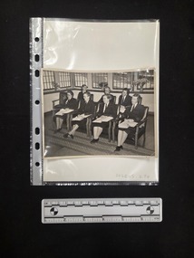Black and white photograph of seven women in uniform seated in two rows. The four women in the front row have folders of paperwork open in their laps. 