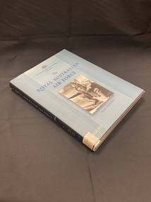 Black hardcover with blue dust-jacket and black spine. Title, author and series title printed along spine, as well as a white label taped to the base with the DDC number typed across it. The front cover is light blue with darker lines running horizontally across. The title is printed in darker blue with a black and white rectangle image of an air force serviceman against a plane, in the centre of the page.