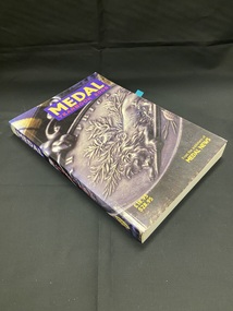 Paperback book, cover image wraps around the spine. 'Medal' printed in yellow text on a purple background at the top of the front cover and spine. Price and publisher printed in yellow at the bottom of the front cover. Large close up image of the South Africa 1877-79 medal covering the cover.