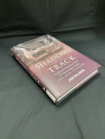 Hardcover with dark purple dust jacket. Title printed in white along the spine and a white spine label sticker at the base. The front cover shows an image of three men carrying another man on a stretcher through thick mud. The lower half of the cover shows the title details in large white print.