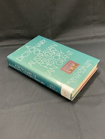 Hardcover book with a dark green dust jacket. Title is printed in white across the cover and spine. There is a small framed illustration of three military men on the lower part of the cover. There is a white spine label sticker at the base of the spine.