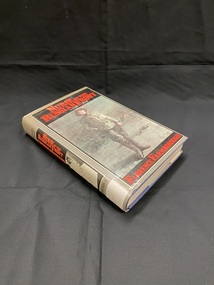 Grey dust-jacket over blue clothbound book.The front cover has a large black rectangle with a white border, the title is printed in red at the top and the author in red text at the bottom. In the centre is a large illustration of an army nurse in a barren field. Along the border is a similar template, however, the nurse is dressed in a white uniform and veil, rather than khaki pants and top.