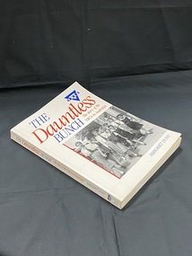 White paperback book . Title on the cover and spine label are royal blue and red. There is a spine label taped to the base of the spine. The front cover contains a black and white photograph of a group of children in pinafores being led by three older girls wearing blouses and ties, down a paved street.