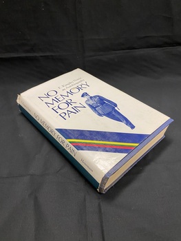 Blue cloth-bound book with white dust-jacket. The spine has a dark green strip running down the left side, the right side is white with green print. The front cover has diagonal blue, yellow,green, pink, blue lines diagonally in the bottom left corner. In the centre is an image of Major Norris in uniform, the title is printed above and around the image in blue print.