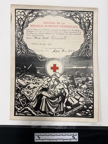 A large board mounted copy of a certificate that has black print artwork of a woman holding a man on her lap in a landscape that has broken wood, ground and a half sunken ship present.  The middle of the certificate has a red cross in a white circle and the top half has text bordered with thorns and foliage.