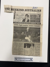 A large newspaper clipping featuring publication name and advertisements for other articles.  The article has a large black and white photo with a smaller photo beneath and five columns of text.  The large photo is of an older woman sitting on the ground, the smaller photo is of the same woman when she was younger.