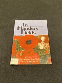 Blue paperback book. Image of red poppies across the lower half wraps around entire cover. White spine label at base of spine attached with tape. Title printed in white along spine. Top half of the front cover has title and author printed in black ink. On the centre right side is a sepia image of a man in uniform.
