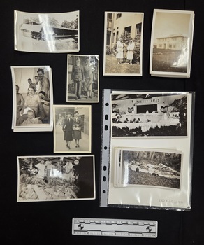 Twenty six black and white photographs of varied sizes printed on gloss photographic paper with white borders. Scenes depicted include individuals in military uniforms at a beach and on a boat, women in nursing uniforms, buildings, and a Christmas display.