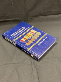 Blue hardback book. Title printed down the spine. Cover has two gold lines across the front, above the top line is the title in white; below the bottom line is the author's name, between the two lines in the middle are a row of six military ribbons and medals.