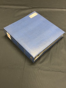 Three ring binder photograph album. The cover is mottled dark blue and black. There are five sets of three gold horizontal lines spaced out down the spine. At the top of the spine is a large white sticker with PA54 in red marker. The top right corner of the front cover has a label with the title handwritten on it in black ink.