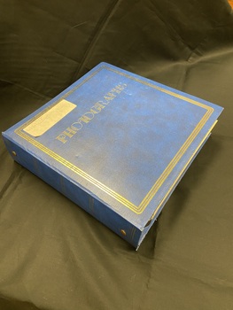 Three ring binder, royal blue, photograph album. Five sets of three horizontal gold lines spaced out down the spine. Triple gold line border around the front cover with the word photographs printed in gold across the cover. Large number of plastic covered, white self-adhesive pages inside.