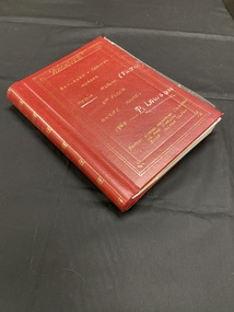 Dark red spiral bound photograph album with gold ornated pattern down the spine. An ornate gold triple line border on the front cover with gold handwriting and additional inscriptions in silver marker.