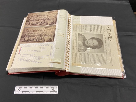 Another example of the page layout, this time showing two photographs and a handwritten note inside the plastic pockets to the left and a newspaper article inserted sideways on the right. Both pages show annotations in the lined memo strips on the inside edges of both sides.