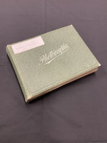 Dark green mottled cover photo album with the word 'photographs' printed across the front cover in white print. There is a white sticker attached to the top left corner with WWI Middle East handwritten on it.